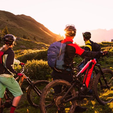 three friends are riding an e-bike withle sunset 